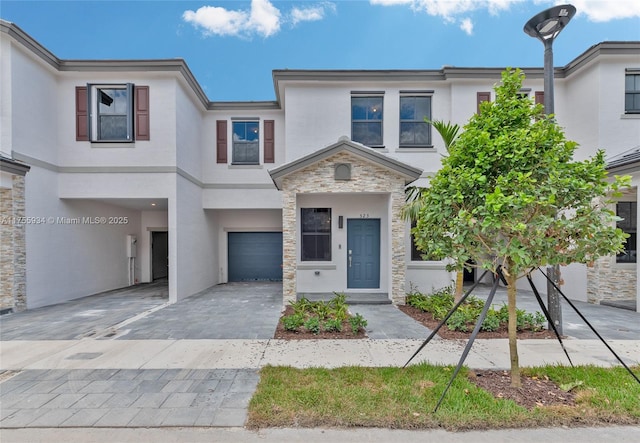 view of property featuring a garage, stone siding, decorative driveway, and stucco siding