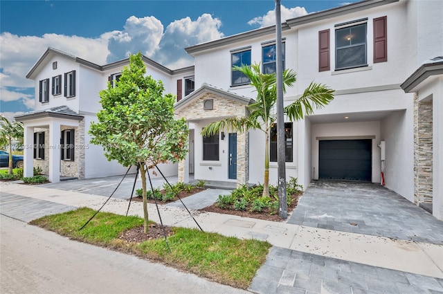 view of front of home featuring decorative driveway, stone siding, a garage, and stucco siding