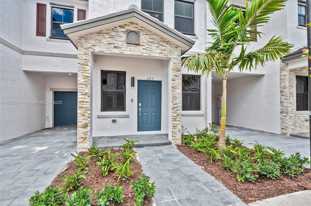 entrance to property with a garage, stone siding, and stucco siding