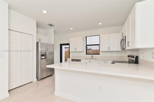 kitchen with stainless steel appliances, light countertops, visible vents, a sink, and a peninsula