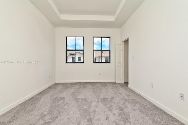 carpeted empty room featuring a raised ceiling and baseboards