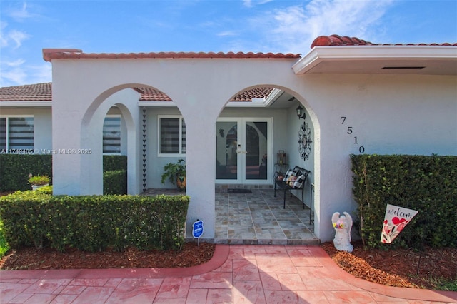 property entrance with french doors, visible vents, a tiled roof, and stucco siding