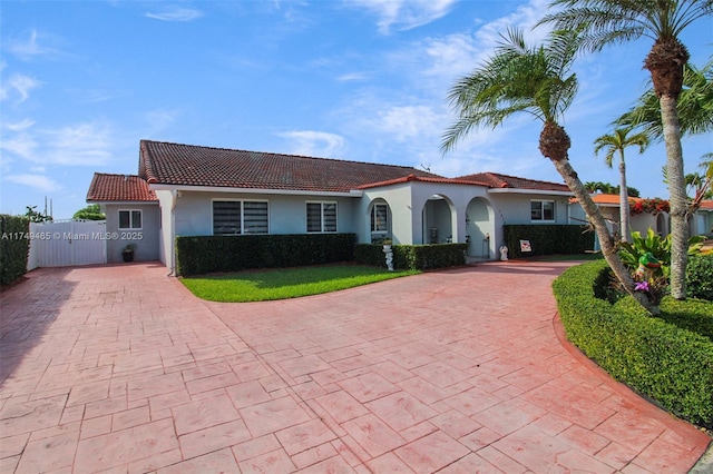 mediterranean / spanish house featuring fence, a tile roof, decorative driveway, a gate, and stucco siding