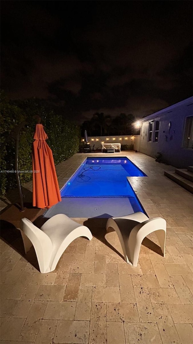 pool at night featuring a patio area