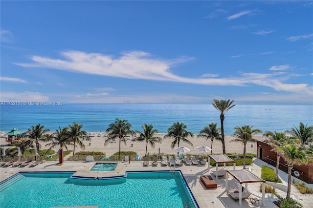 pool with a patio, a water view, and a hot tub