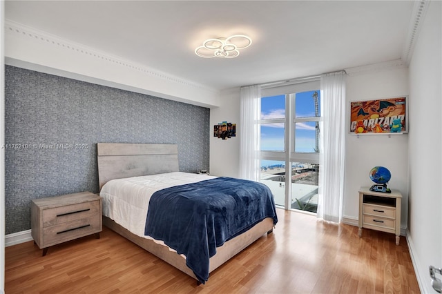 bedroom with an accent wall, crown molding, light wood-style flooring, and baseboards