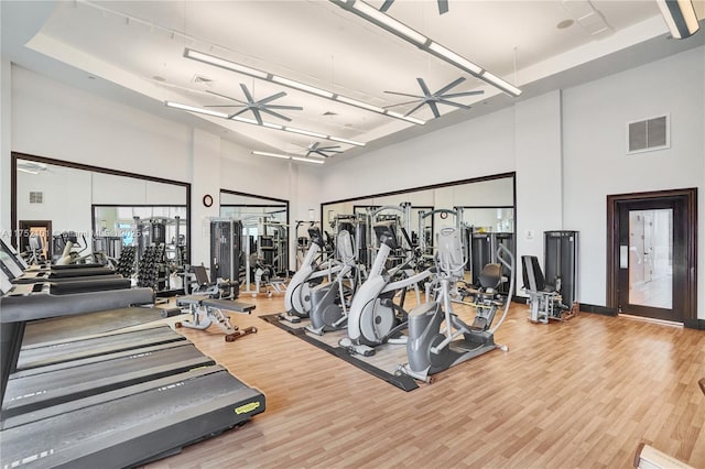 exercise room featuring a ceiling fan, visible vents, a high ceiling, and wood finished floors