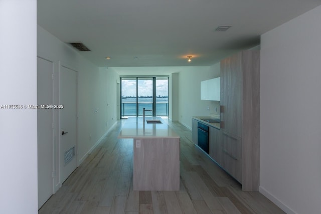 kitchen with light wood finished floors, visible vents, an island with sink, modern cabinets, and light countertops