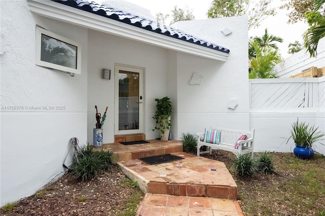 doorway to property with fence, a tiled roof, and stucco siding