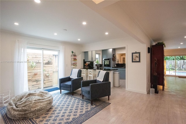 living room featuring light wood-style floors, baseboards, ornamental molding, and recessed lighting