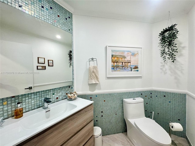 bathroom with a wainscoted wall, crown molding, tile walls, toilet, and vanity