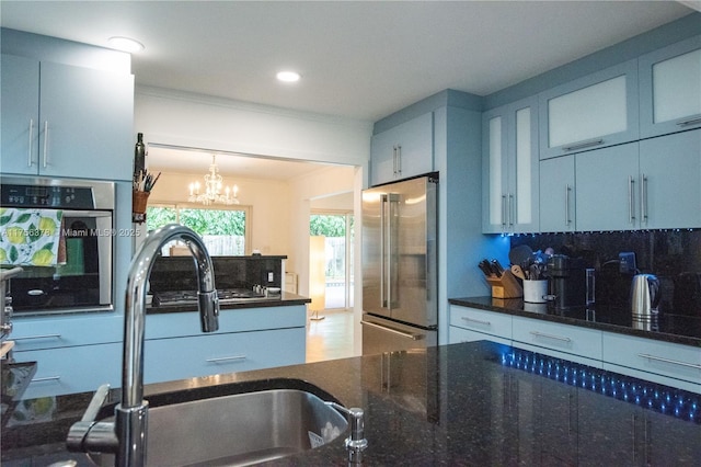 kitchen with crown molding, stainless steel appliances, decorative backsplash, a sink, and dark stone countertops