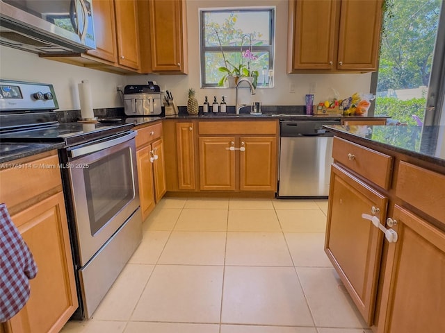 686 NE 191st Ter, Miami, FL 33179 - kitchen with stainless steel appliances, a sink, brown cabinetry, light tile patterned floors, and dark stone counters