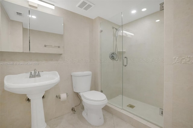 bathroom with toilet, a shower stall, visible vents, and tile walls