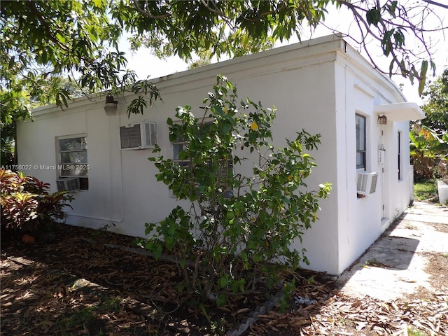 view of property exterior with a wall unit AC, cooling unit, and stucco siding