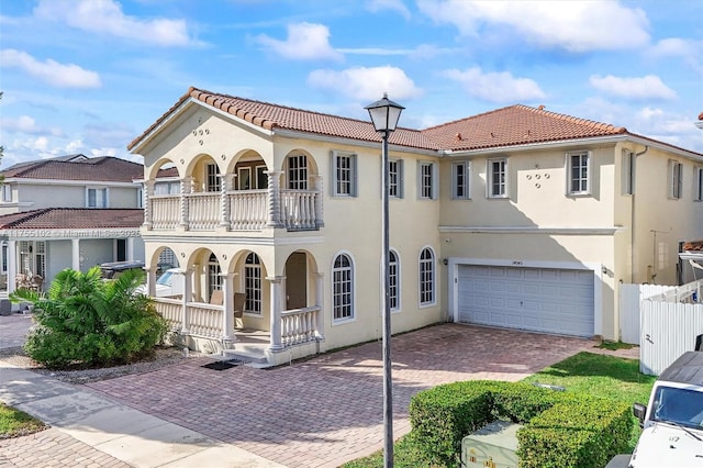 mediterranean / spanish-style house with decorative driveway, stucco siding, a porch, an attached garage, and a balcony