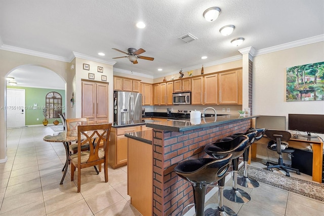 kitchen featuring arched walkways, light tile patterned floors, stainless steel appliances, dark countertops, and a peninsula