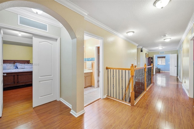 hall featuring light wood-style floors, visible vents, arched walkways, and crown molding