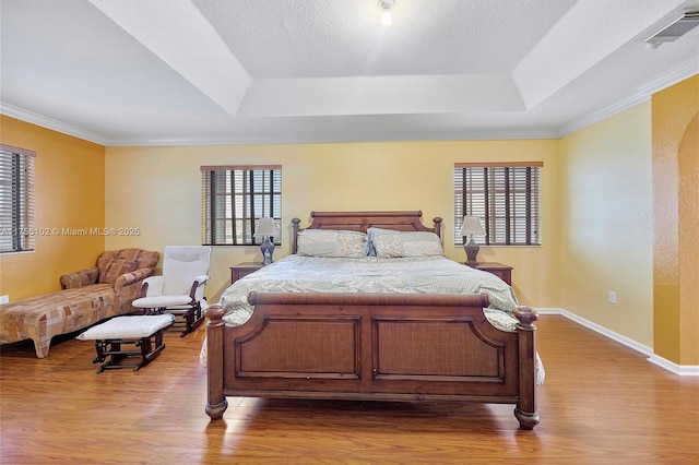 bedroom featuring wood finished floors, visible vents, a raised ceiling, and multiple windows