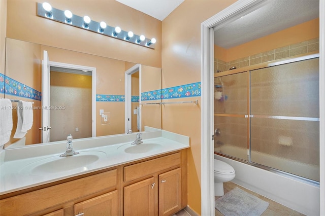 bathroom with combined bath / shower with glass door, a sink, toilet, and double vanity