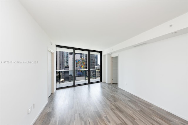 spare room featuring light wood-style flooring, visible vents, floor to ceiling windows, and baseboards