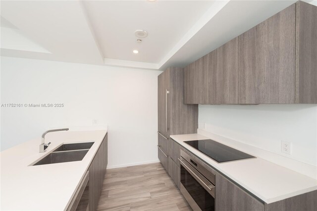 kitchen with wall oven, modern cabinets, black electric cooktop, and a sink