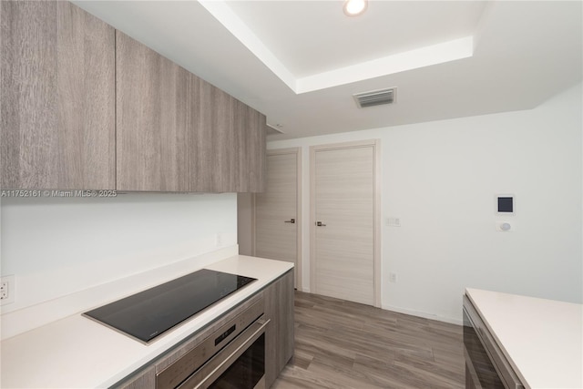 kitchen featuring wall oven, visible vents, modern cabinets, black electric cooktop, and light countertops