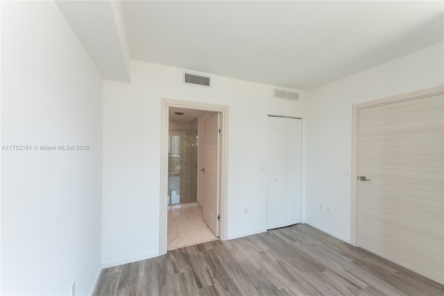 unfurnished bedroom featuring visible vents, connected bathroom, baseboards, and wood finished floors