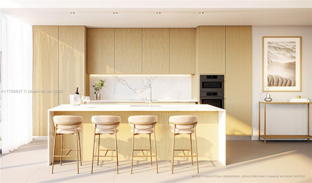 kitchen with a kitchen island with sink, light countertops, stainless steel double oven, and a kitchen breakfast bar