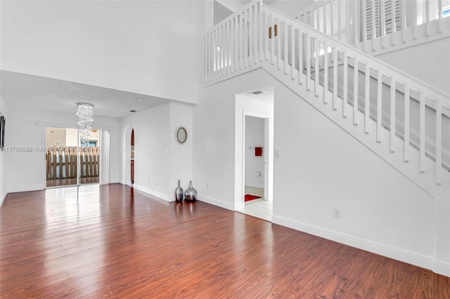 unfurnished living room featuring stairs, a chandelier, baseboards, and wood finished floors