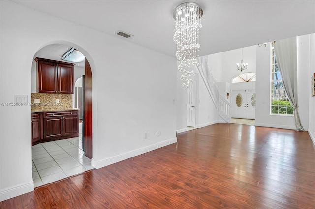 unfurnished living room featuring baseboards, visible vents, arched walkways, light wood-type flooring, and a notable chandelier