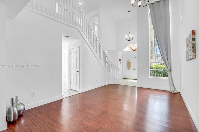 entrance foyer with a notable chandelier, visible vents, a towering ceiling, wood finished floors, and stairs