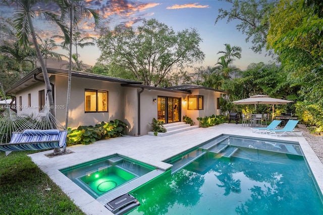 back of property at dusk with a pool with connected hot tub, a patio area, and stucco siding