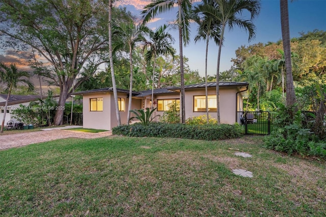 view of front of home featuring a gate, a lawn, a standing seam roof, and stucco siding