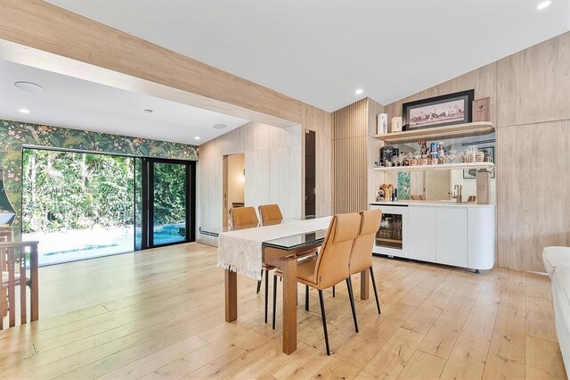 dining area featuring lofted ceiling, wine cooler, bar, a baseboard heating unit, and light wood finished floors