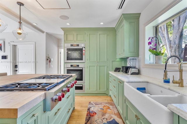 kitchen featuring light wood finished floors, visible vents, appliances with stainless steel finishes, a sink, and green cabinetry