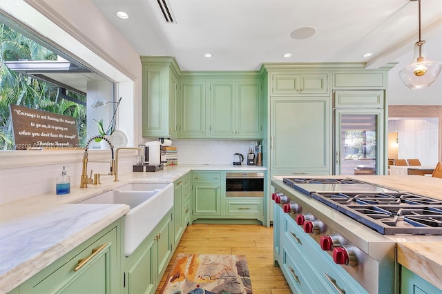 kitchen featuring stainless steel gas stovetop, decorative backsplash, light wood-style floors, a sink, and green cabinetry