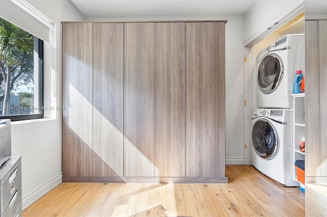 laundry room with light wood-type flooring, laundry area, baseboards, and stacked washer and clothes dryer