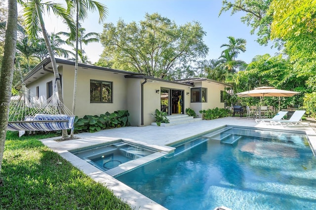 rear view of house with an outdoor pool, an in ground hot tub, a patio area, and stucco siding