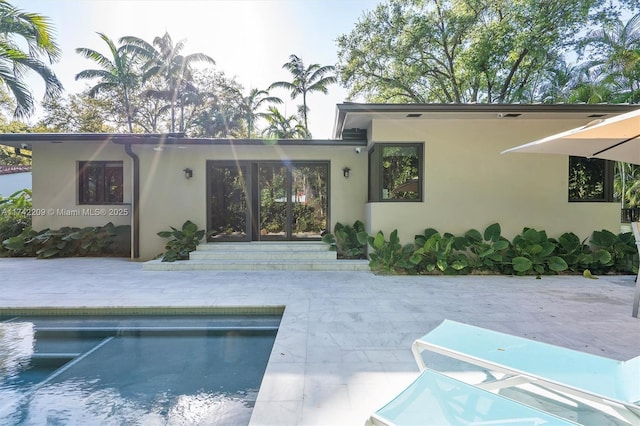 back of property with french doors, a patio area, an outdoor pool, and stucco siding