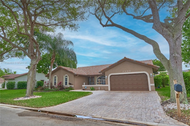 view of front of house featuring a tiled roof, an attached garage, decorative driveway, a front yard, and stucco siding