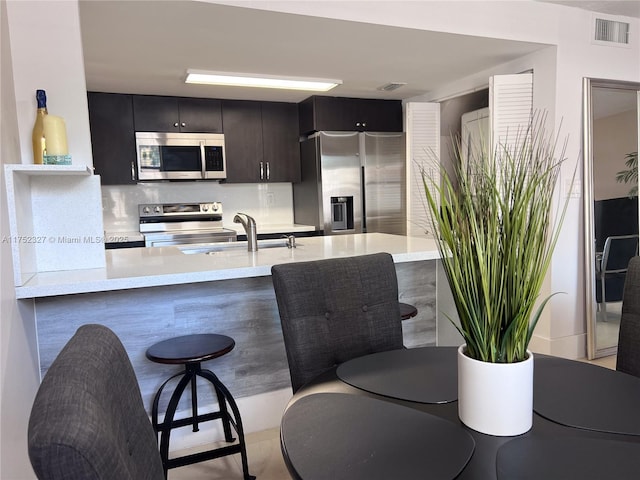 kitchen featuring visible vents, a peninsula, a sink, stainless steel appliances, and a kitchen breakfast bar