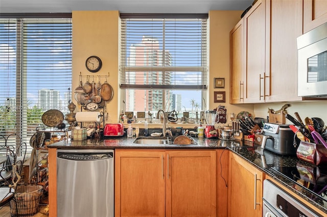 kitchen with white microwave, wall oven, a sink, stainless steel dishwasher, and dark stone counters