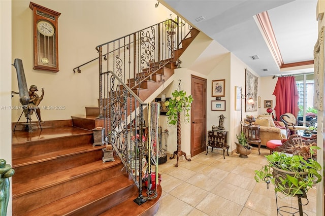 stairway with tile patterned flooring, visible vents, ornamental molding, and a tray ceiling