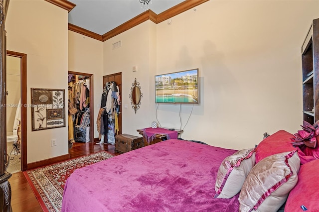 bedroom with a walk in closet, a closet, ornamental molding, wood finished floors, and baseboards