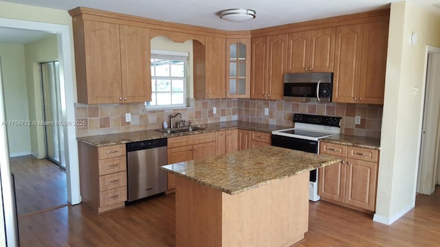 kitchen featuring light wood finished floors, decorative backsplash, light stone countertops, stainless steel appliances, and a sink