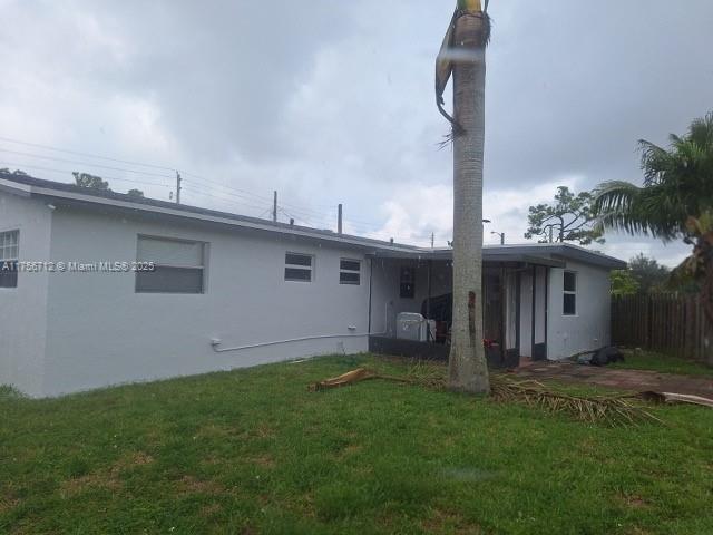 rear view of house featuring stucco siding, fence, and a yard