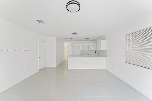 unfurnished living room with visible vents, a sink, baseboards, and light tile patterned flooring