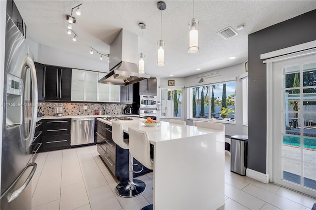 kitchen with stainless steel appliances, island range hood, light countertops, decorative backsplash, and dark cabinets