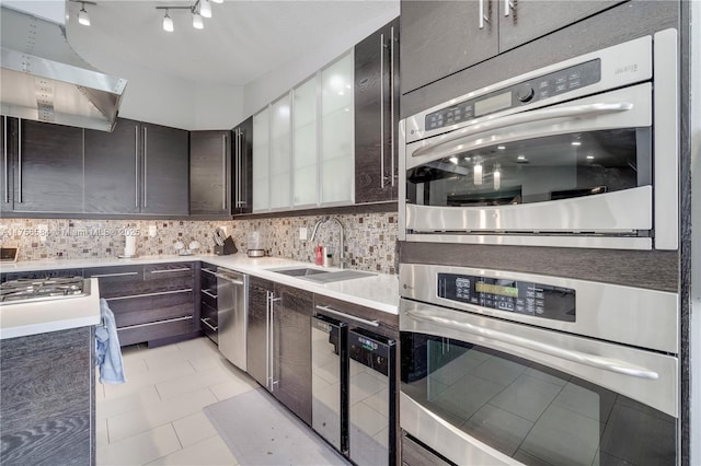 kitchen featuring a sink, backsplash, range hood, stainless steel appliances, and light countertops